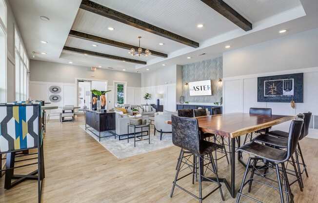 Downtown Greenville, SC Apartments - The Aster - Resident Clubroom with High Ceilings, Vinyl Plank Flooring, Area Rug, Mounted Television, Seating Area, Table, and Chairs.
