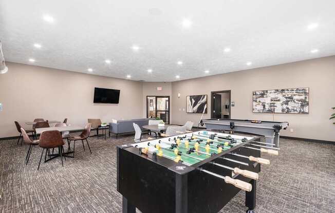 A foosball table is in the middle of a room with chairs and a TV.