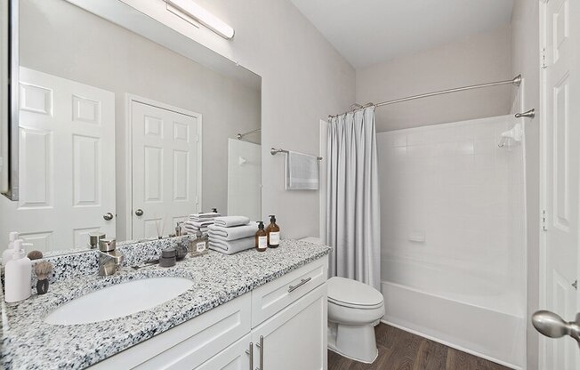 Model Bathroom with White Cabinets, Wood-Style Flooring and Shower/Tub at Chapel Hill Apartments in Lewisville, TX.