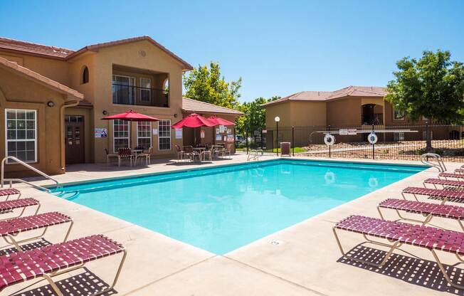 A swimming pool surrounded by red sunshades and lounge chairs at West Park Apartments, Albuquerque, NM