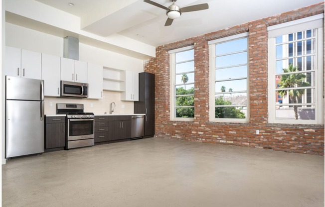 apartment unit kitchen with stainless steel appliances and a brick wall with large windows.