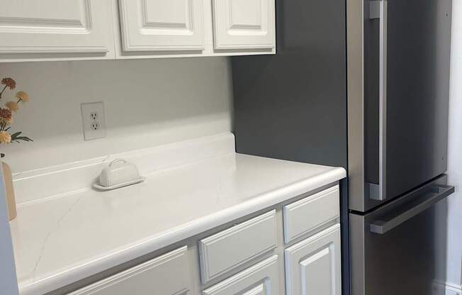 A black refrigerator stands next to a white countertop and cabinets.