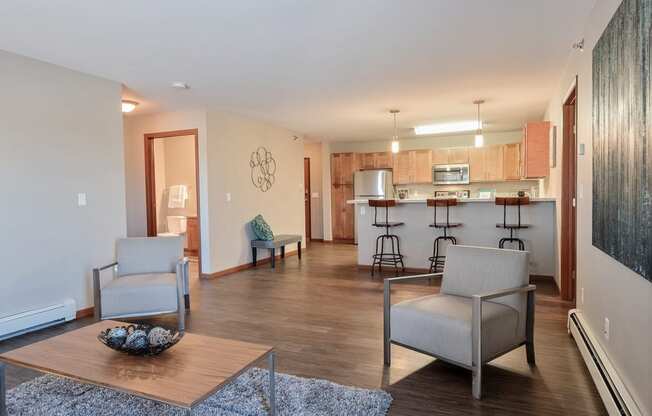 a living room with two chairs and a table in front of a kitchen. Fargo, ND Urban Plains Apartments
