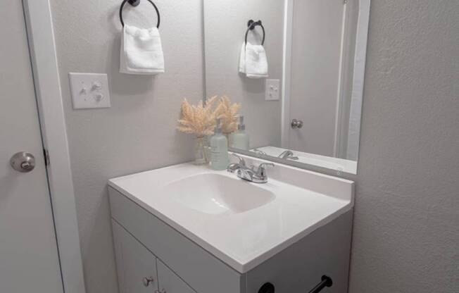 A white bathroom sink with a vase of dried flowers on top.