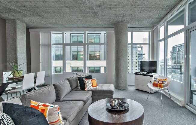 a living room with a gray couch and a tv in a room with large windows