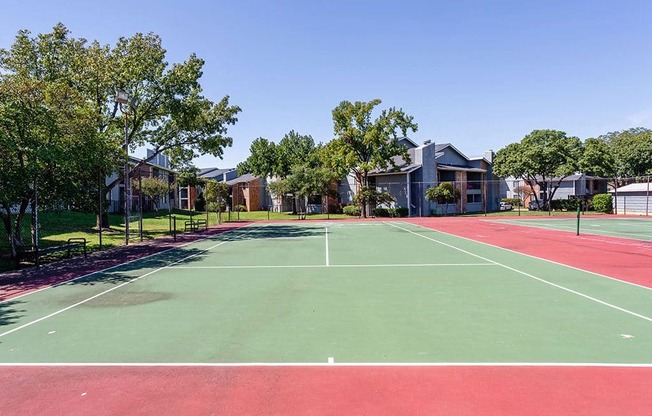 a tennis court with trees and apartments in the background