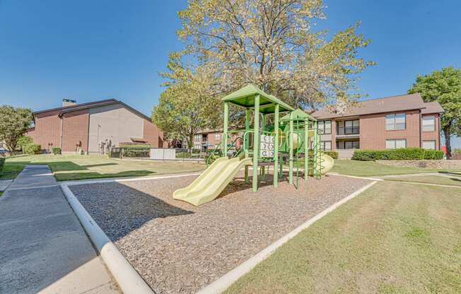 A playground with a green slide in front of a red brick building.