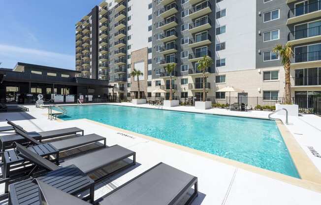 a swimming pool with lounge chairs in front of an apartment building