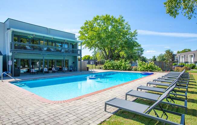 A pool with a building behind it and benches along the side.