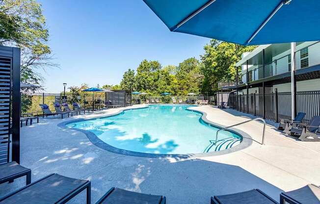A large outdoor swimming pool surrounded by lounge chairs and trees.