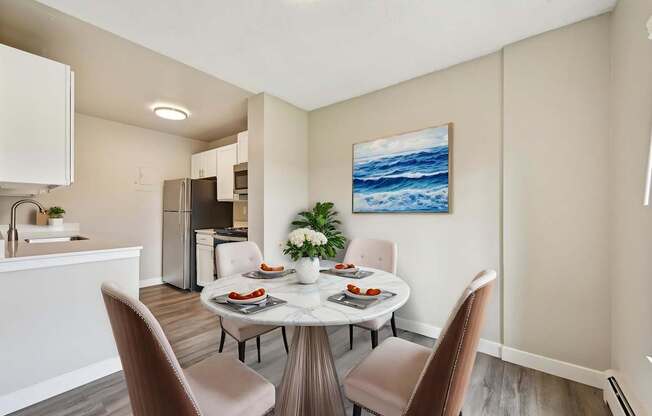 A dining room with a table set for two and a painting of the ocean on the wall.