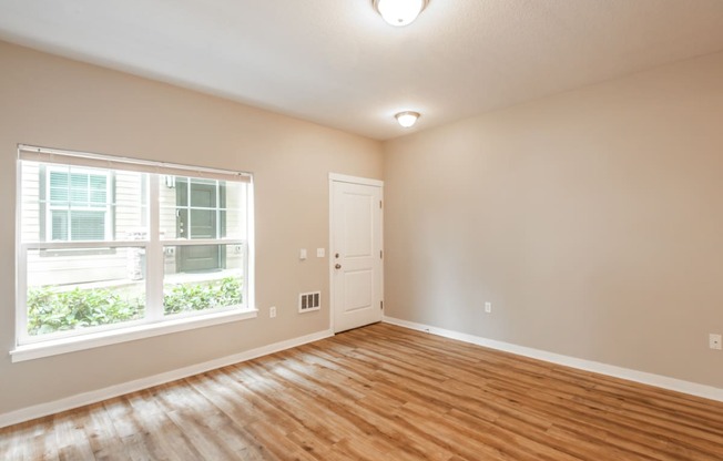 an empty living room with a large window and wood flooring