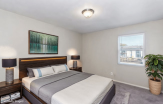 A bedroom with a large bed, two lamps, a painting, and a potted plant.