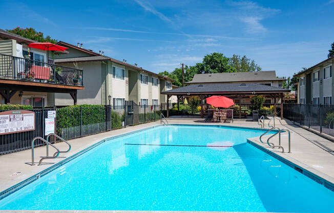 View of gated community pool with seating under umbrellas and covered area with seating and picnic table