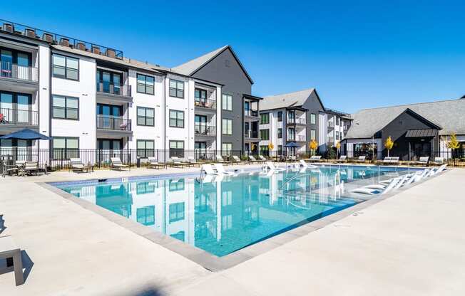 Dog-Friendly Apartments In Huntsville, AL - The Collins - Gated Resort-Style Salt Water Pool with Poolside and Submerged Lounge Seats, Tables, Chairs, Umbrellas, and View of Apartment Buildings