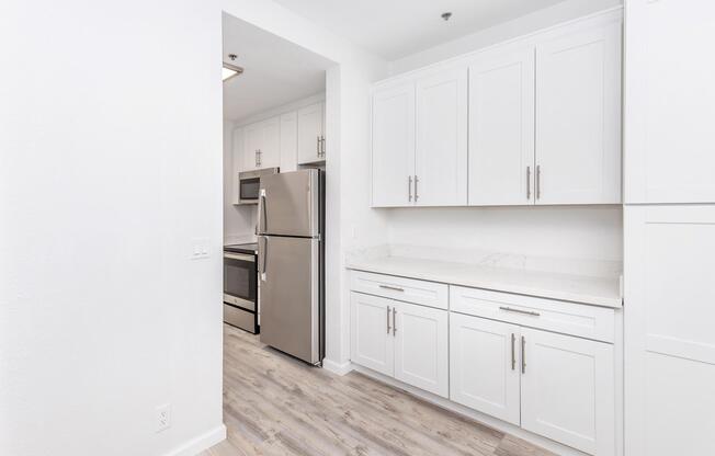 Modern kitchen with white cabinetry, stainless steel refrigerator, and an electric stove. Light wood-like flooring complements the bright, minimalist design. The space features a marble countertop and ample storage, creating a clean and inviting atmosphere.