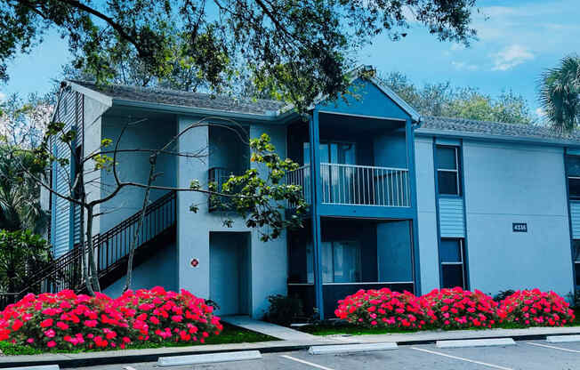 A blue apartment building with a parking lot and flowers at Aqua Bay Apartments in Naples, FL 34116