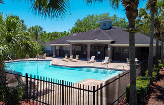 Swimming pool with lounge seating surrounded by palm trees and clubhouse in the background