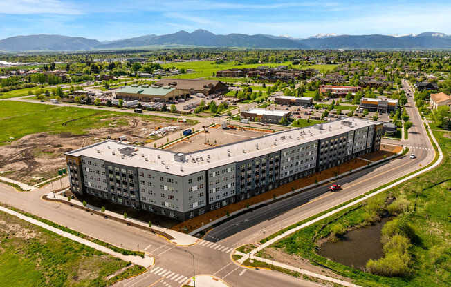 A large grey building is surrounded by a grassy area and a road with cars.