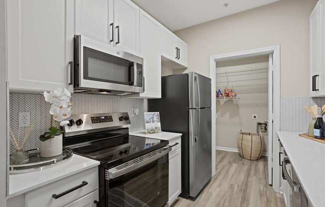 Flatiron West Trade Apartments staged model unit kitchen connected to living room with stainless steel modern appliances and quartz countertops