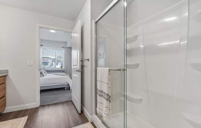 a white bathroom with a glass shower and a bedroom
