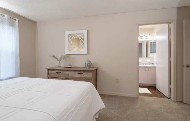 a bedroom with a white bed and a bathroom with a sink