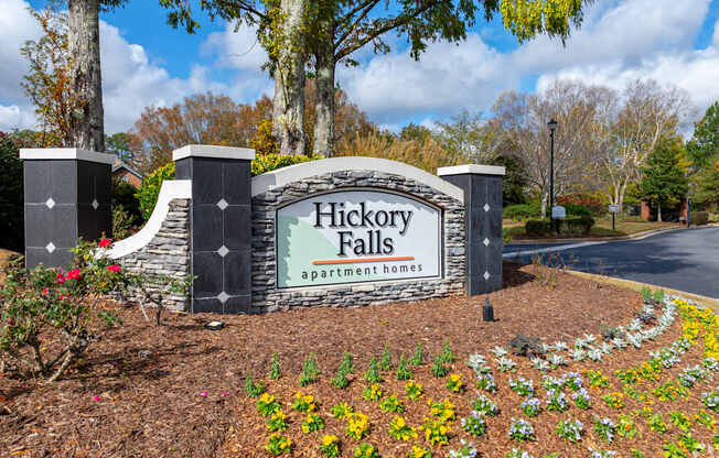 A sign for Hickory Falls Apartment Homes is surrounded by flowers and trees.