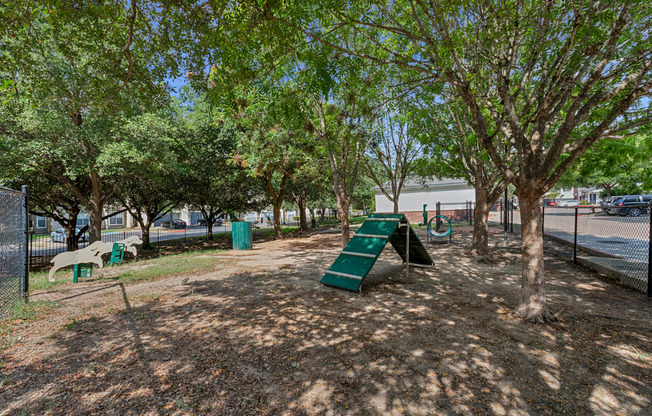 A playground with a green slide and trees.