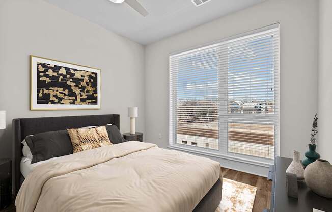 A bedroom with a bed, pillows, a ceiling fan, and a painting on the wall.