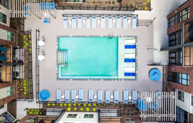 A large rectangular pool is surrounded by a white fence and blue loungers.