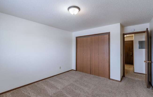 a room with a carpeted floor and a door to a hallway. Fargo, ND Plumtree Apartments