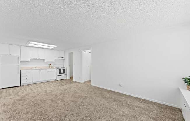 an empty living room and kitchen with white cabinets and white appliances