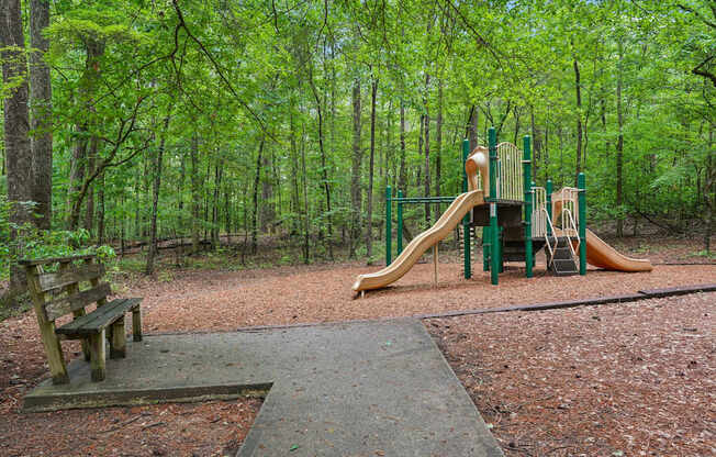 A playground with a slide and a bench in a wooded area.
