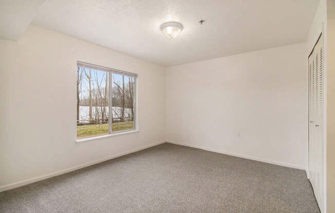 A bedroom with a large window and a carpeted floor at West Hampton Park Apartments in Elkhorn, NE 68022