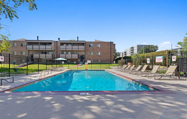 A swimming pool surrounded by chairs and a building in the background.