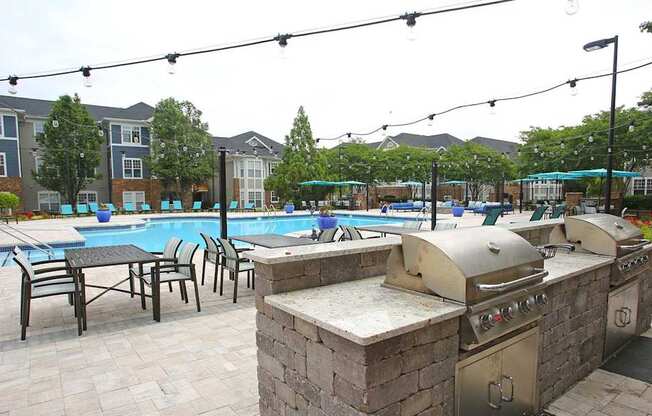 A pool with a barbecue grill and chairs is surrounded by apartment buildings.