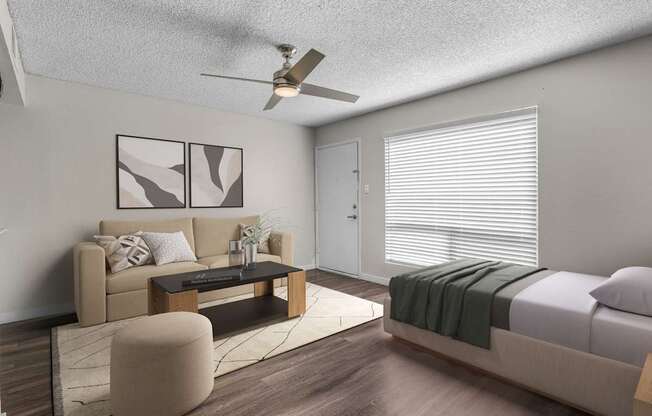 A modern living room with a beige sofa, a coffee table, and a bed with a green blanket.