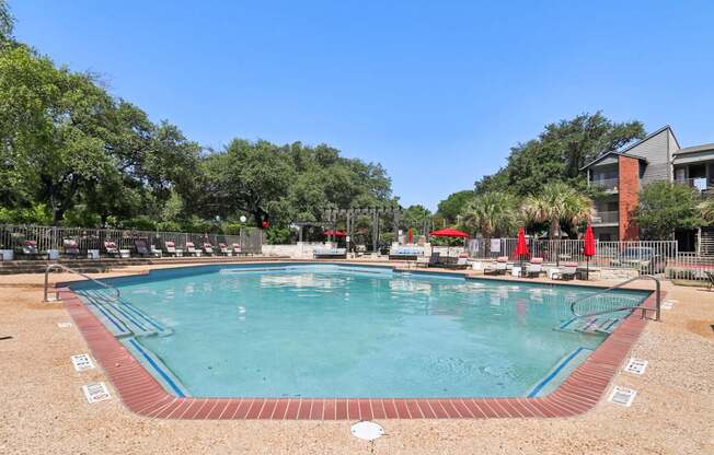 A large outdoor swimming pool surrounded by trees and a fence.