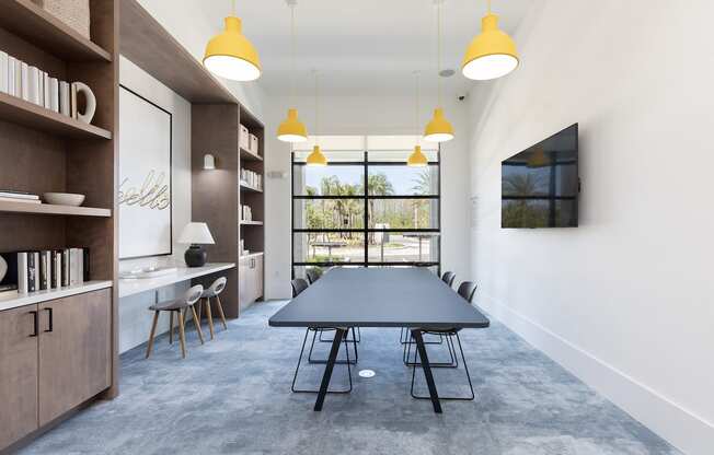 large common room with chairs, table, bookshelves, TV, and large windows