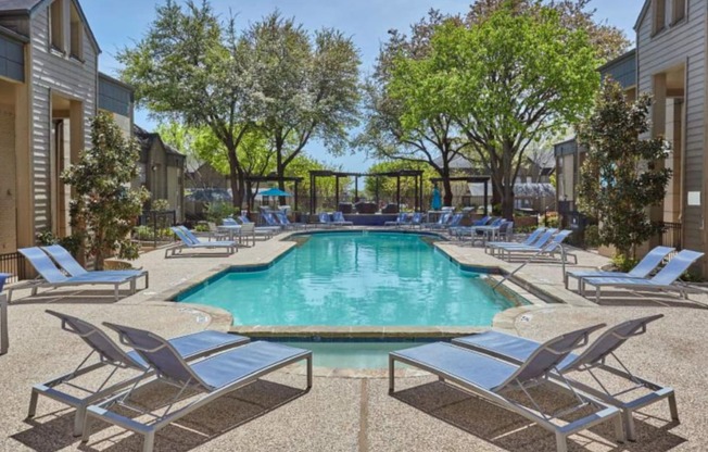 a swimming pool with chaise lounge chairs and trees in the background