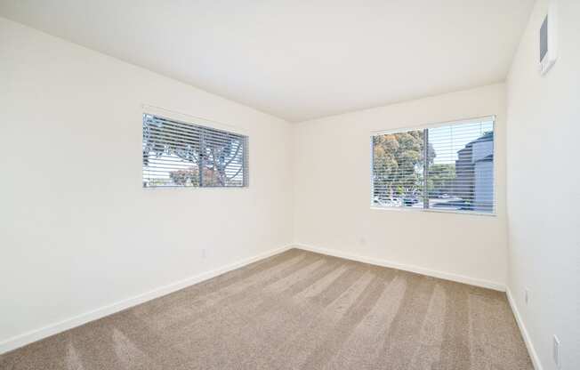 an empty room with carpet and two windows