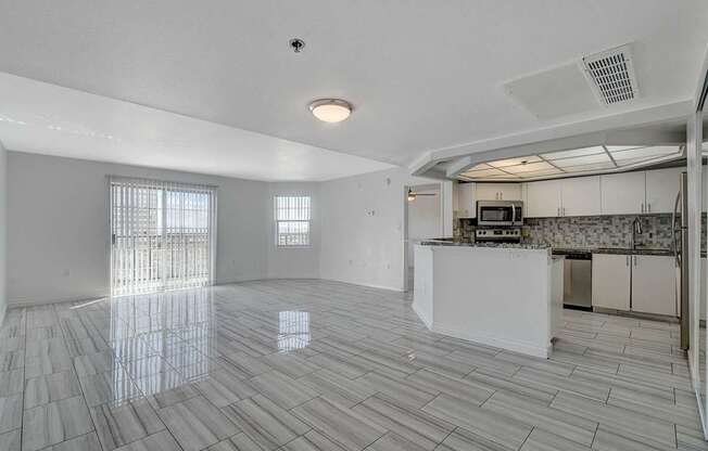 A spacious kitchen and living room with white tiled floors and a large window.