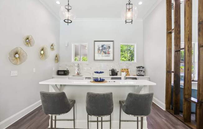 A white dining table with four grey chairs and a chandelier hangs above it.
