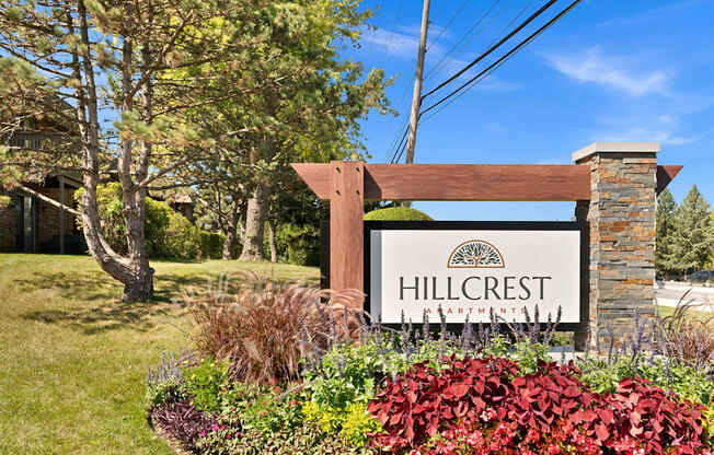 a sign for hillcrest apartments in front of a garden and trees