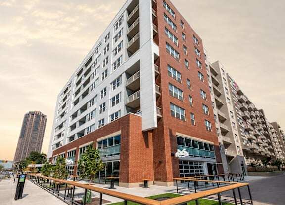 A modern multi-story building with a red brick facade and a balcony with a wooden railing.
