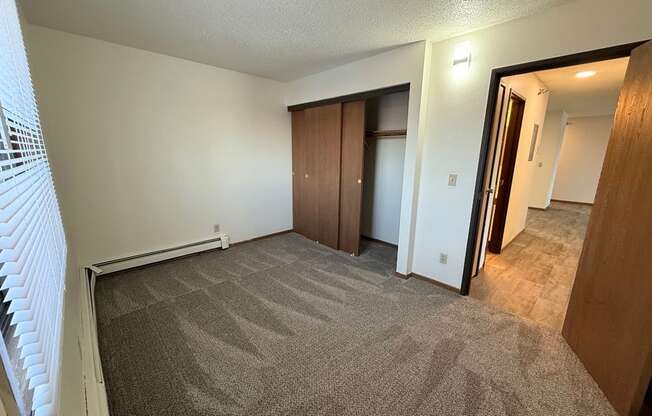A room with carpeted floor and a window with blinds.