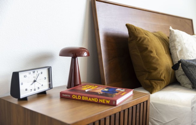 a clock and a book on a night stand next to a bed at Analog PDX Apartments, Oregon 97227