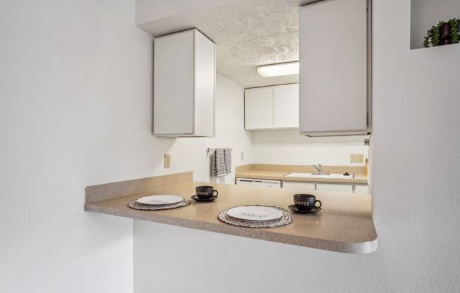 a kitchen with white cabinets and a counter with plates and mugs