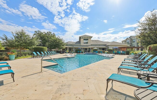 A sunny day at the pool with lounge chairs and a building in the background.