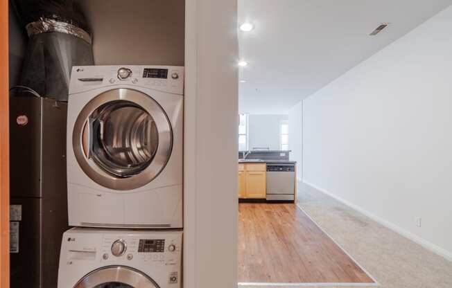 a washer and dryer in a laundry room with a kitchen in the background at 26 West, Managed by Buckingham Urban Living, Indianapolis